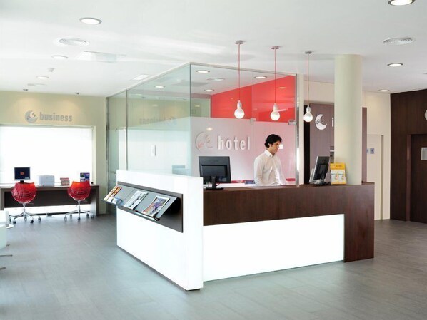 A hotel reception area with a glass partition, a reception desk, and a computer monitor.