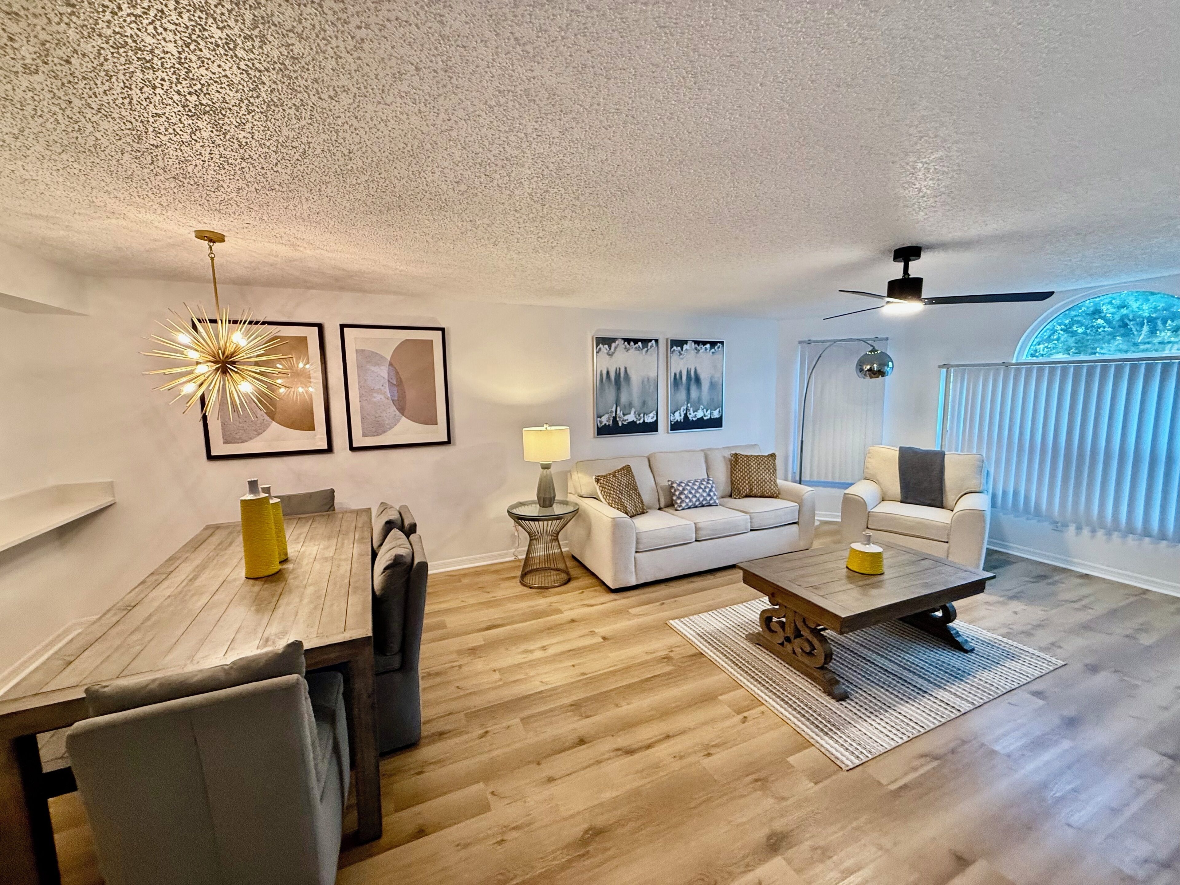 A modern living room with a dining area, two sofas, a coffee table, and a ceiling fan.