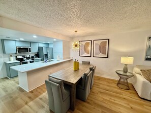 A modern kitchen with a central island, dining area with chairs, a sofa, and a small side table.