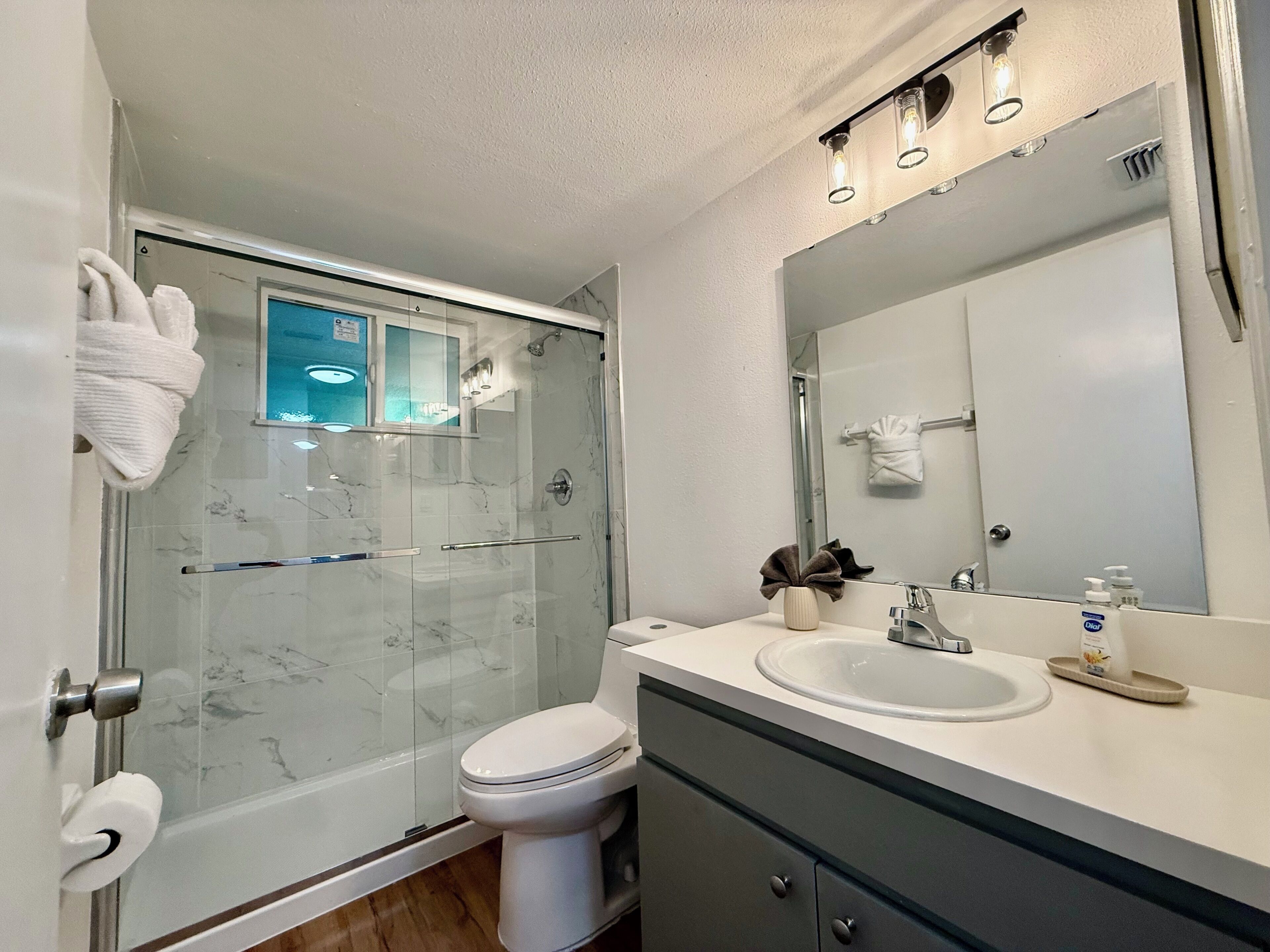 A modern bathroom with a glass-enclosed shower, a white toilet, a sink with a mirror, and a towel rack.