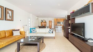 A modern living room with a sofa, coffee table, and TV. There is a kitchen in the background with a dining area. - Stylish Villa for rent with 4 bedrooms and swimming pool on a wide channel in Empuriabrava (Empuria Brava)