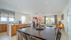 A modern kitchen with a central island, wooden cabinets, and a dining area with a dark wooden table and chairs. - Stylish Villa for rent with 4 bedrooms and swimming pool on a wide channel in Empuriabrava (Empuria Brava)