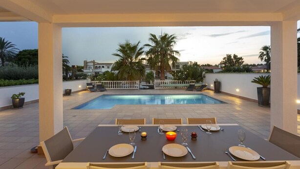 A dining area with a pool view, outdoor seating, and a sunset backdrop. - Stylish Villa for rent with 4 bedrooms and swimming pool on a wide channel in Empuriabrava (Empuria Brava)
