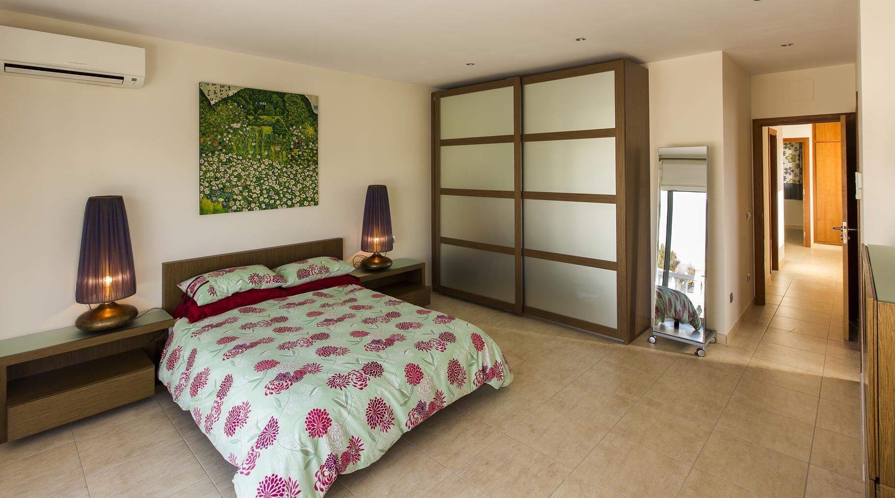 A bedroom with a bed, bedside lamps, a large mirror, and a sliding door closet.