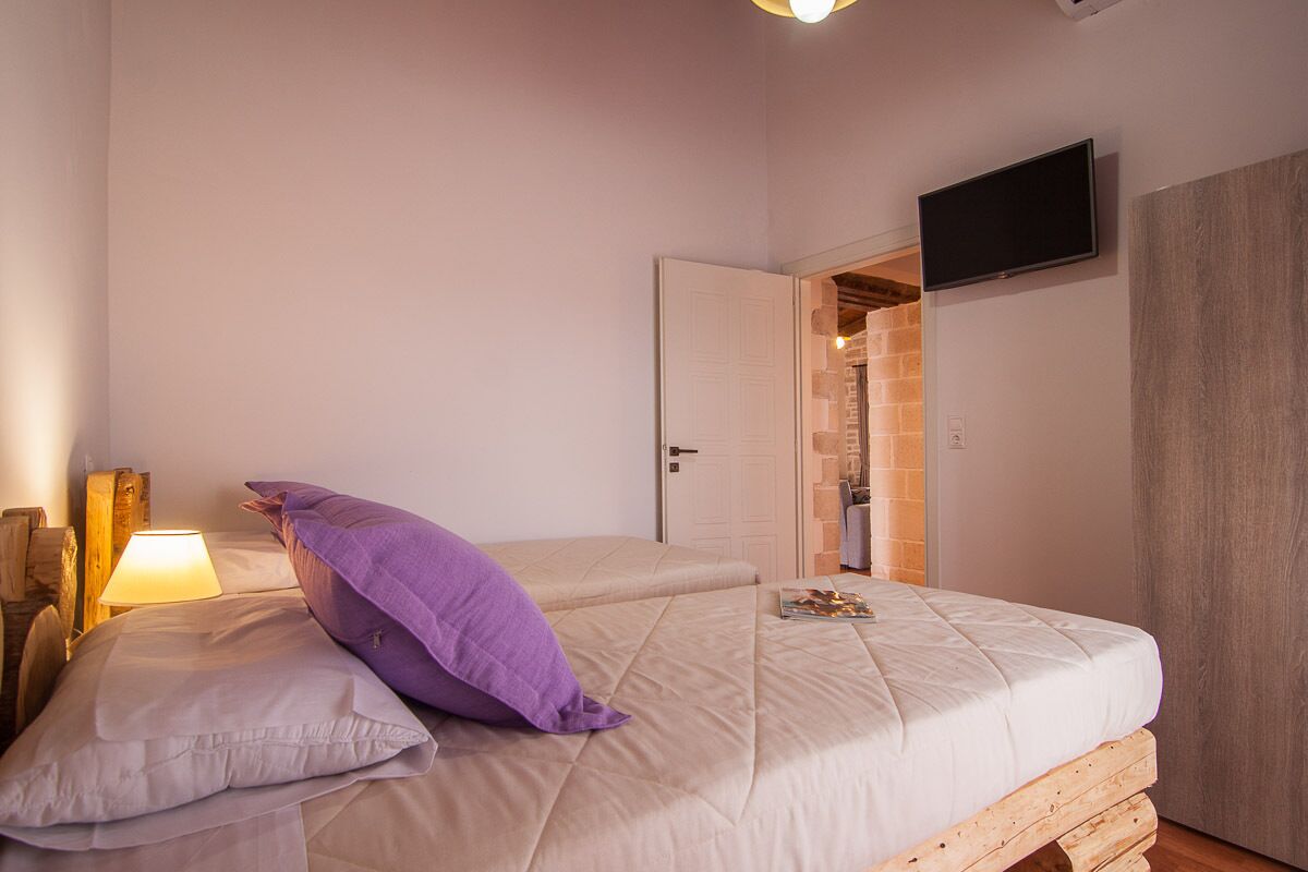 A bedroom with a bed, a TV mounted on the wall, and a door leading to another room.