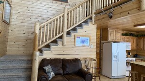 A wooden interior with a staircase, a brown leather sofa, and a kitchen area. - Comfortable cozy cabin, accessible to Snowmobile & ATV trails & Fly Fishing  (Island Park)