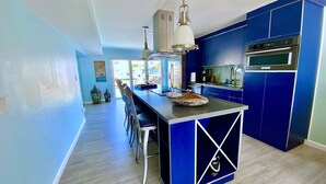 Une cuisine moderne avec des meubles bleus, un îlot central, des appareils en acier inoxydable et des luminaires suspendus.