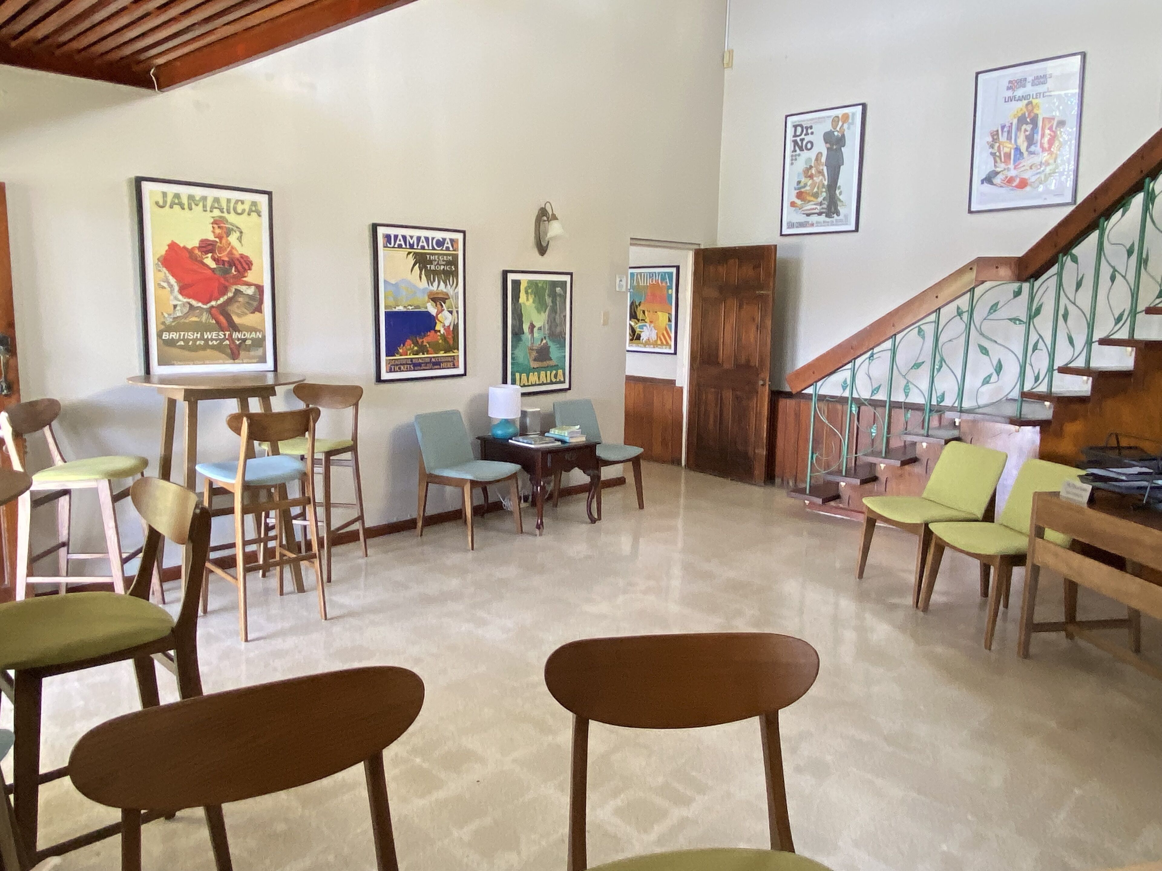 A hotel lobby with wooden chairs, a staircase, and several Jamaica-themed posters on the walls.