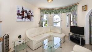 A modern living room with a white leather sofa, a glass coffee table, a flat-screen TV, and a painting on the wall. - House with 3 bedrooms and pool overlooking the lake (Empuria Brava)