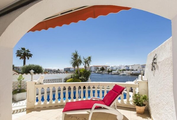 A balcony with a white railing, a red cushion, and a view of the sea and buildings.