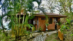A rustic house with a tiled pathway leading to the entrance, surrounded by lush greenery and palm trees. - Montezuma Heights the cute Mariposa Cottage, into the great wide open.  Sleeps 2 (Montezuma)