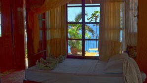 A room with a bed, a fan, and a view of palm trees through a window. - Montezuma Heights the cute Mariposa Cottage, into the great wide open.  Sleeps 2 (Montezuma)