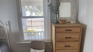Une pièce avec une fenêtre, une commode en bois dotée de tiroirs, une chaise avec un coussin à motifs et un miroir décoratif orné de motifs floraux.