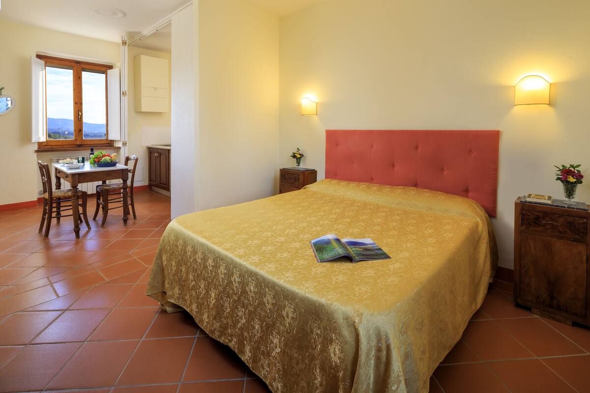 Ein Schlafzimmer mit einem großen Bett, einem Esstisch mit Stühlen, einem Fenster und einem kleinen Tisch mit einer Vase.