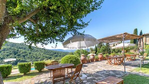 An outdoor patio with stone flooring, wooden furniture, and large umbrellas providing shade. - Fattoria Santo Stefano - Agriturismo (Greve in Chianti)
