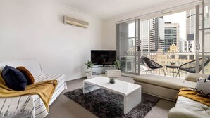 A modern living room with a white sofa, a white coffee table, and a TV. There is a large window with a city view. - A Stylish & Comfy Apt Next to Darling Harbour (Sydney)