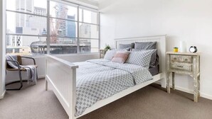 A bedroom with a bed, a chair, a nightstand, and a window with a city view. - A Stylish & Comfy Apt Next to Darling Harbour (Sydney)