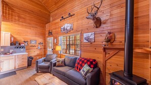 Ein gemütliches Blockhaus-Interieur mit Kamin, Holzwänden, einer Couch und einer Küchenzeile.