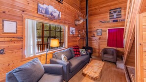 Ein gemütliches Blockhaus-Interieur mit Holzausstattung, einer Couch, einem Sessel, einem Kamin und Hirschgeweihen an der Wand.