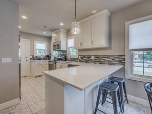 A modern kitchen with white cabinetry, a large island, and a view of the street.