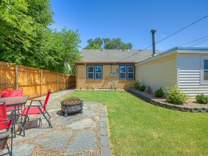 A backyard with a stone patio, a fire pit, a wooden fence, and a yellow house.