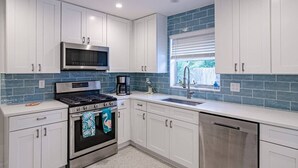 Una cocina moderna con armarios blancos, una estufa de acero inoxidable, un microondas y una ventana con persianas.