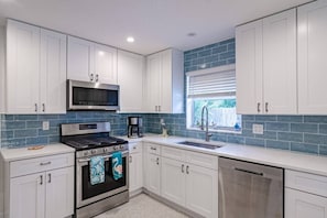 Une cuisine moderne avec des meubles blancs, une cuisinière en acier inoxydable, un four à micro-ondes et une fenêtre avec des stores.