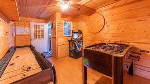 A wooden-floored room with a shuffleboard table, a foosball table, and a dartboard.