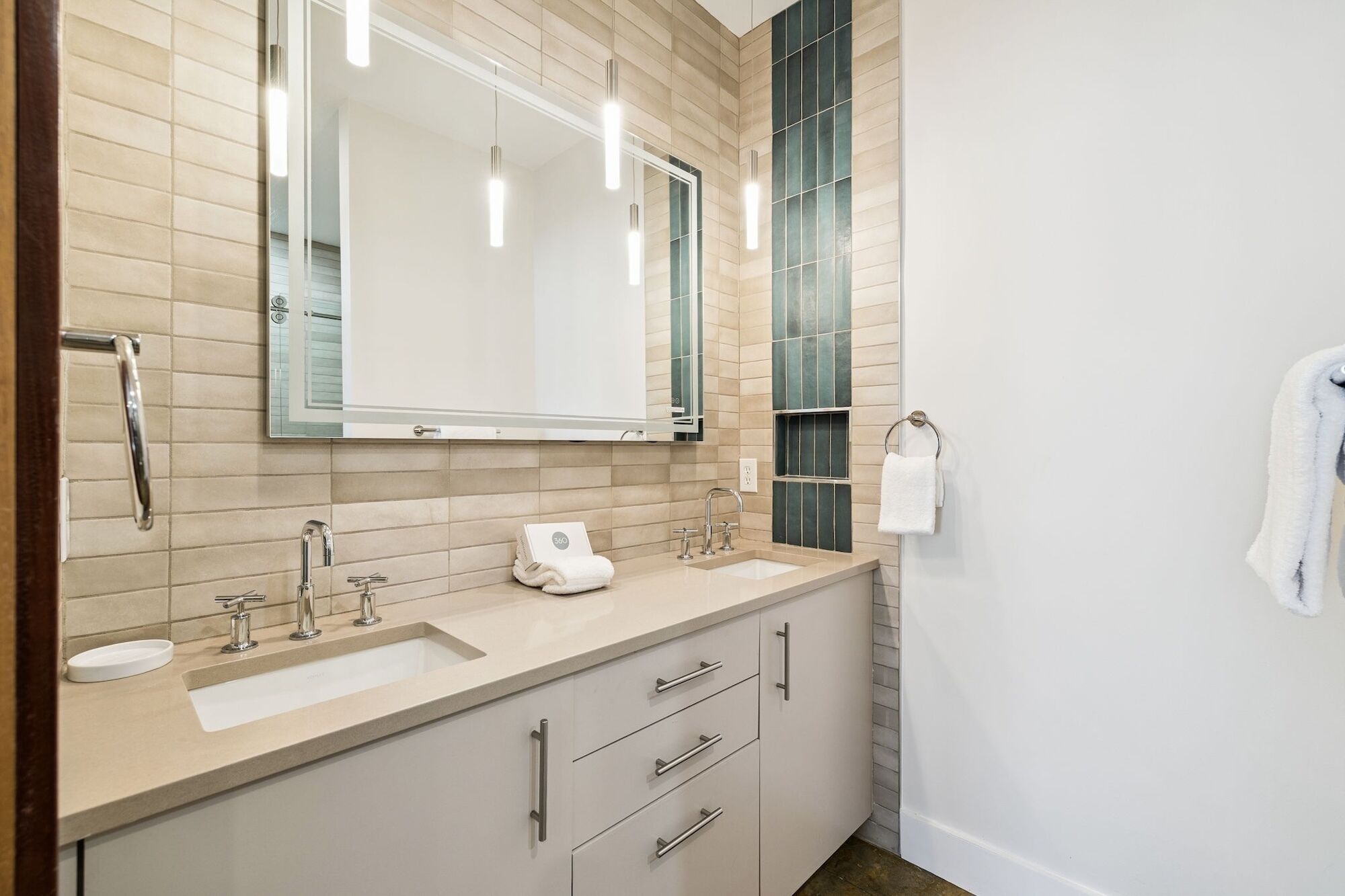 A modern bathroom with two sinks, a large mirror, and a towel rack.