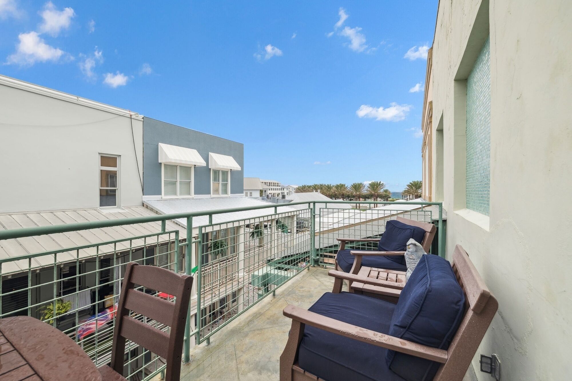 A balcony with two lounge chairs and a small table, overlooking a building with a white facade and a blue roof.