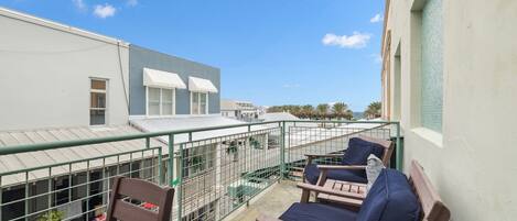 A balcony with two lounge chairs and a small table, overlooking a building with a white facade and a blue roof.