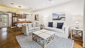 A modern living room with a sofa, coffee table, and lamps. There is a kitchen in the background with a refrigerator and cabinets. - Walk to Beach and Town Square w/ Gulf Views (Santa Rosa Beach)