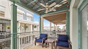 A covered balcony with two blue cushioned chairs and a small table, overlooking a street with parked cars and buildings. - Walk to Beach and Town Square w/ Gulf Views (Santa Rosa Beach)