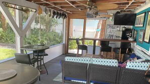 Een overdekt terras met een tafel, stoelen, een bank en een televisie.