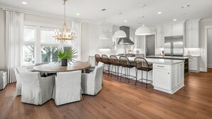 A modern kitchen with white cabinetry, a central island, and a dining area with a round table and chairs. - Close to the Town Square w/ Pool and LSV (Seacrest Beach)
