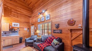 A cozy cabin interior with a wooden interior, a fireplace, a sofa with a blanket, and a kitchen area. - Black Bear Cabin-onsite "bear hunt" & playground, game room, kitchen AC & heat (Payson)