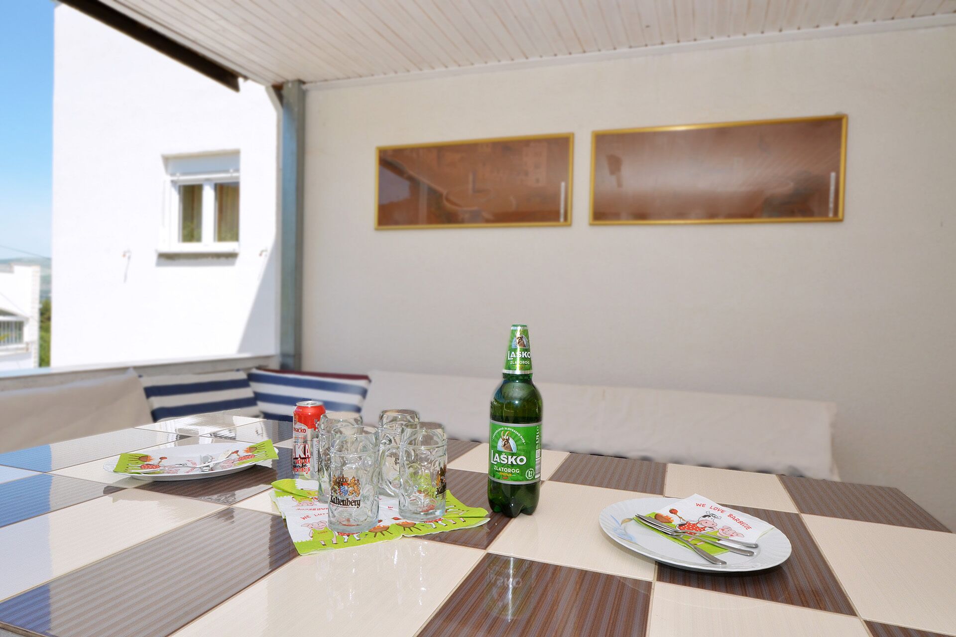 Ein Esstisch mit Tellern, Besteck und einer Bierflasche auf einem Balkon mit Blick auf Gebäude.