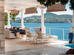 Une terrasse meublée de mobilier en osier, une table dressée pour le repas et une vue sur un lac.