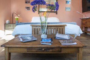 A bedroom with a bed, a wooden nightstand, a bedside table with magazines and a guest book, and a vase with flowers. - Escape into serenity just minutes from the Plaza. Hot tub and sauna. (Santa Fe)