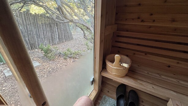 Una cabaña de madera con puerta de madera, un estante pequeño con un cuenco de madera, y un par de zapatos negros en el suelo.