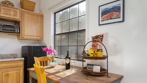 Una cocina con armarios de madera, un refrigerador negro, un microondas, una mesa de comedor de madera con sillas, un jarrón con flores, una botella de vino y un calendario sobre un soporte metálico.