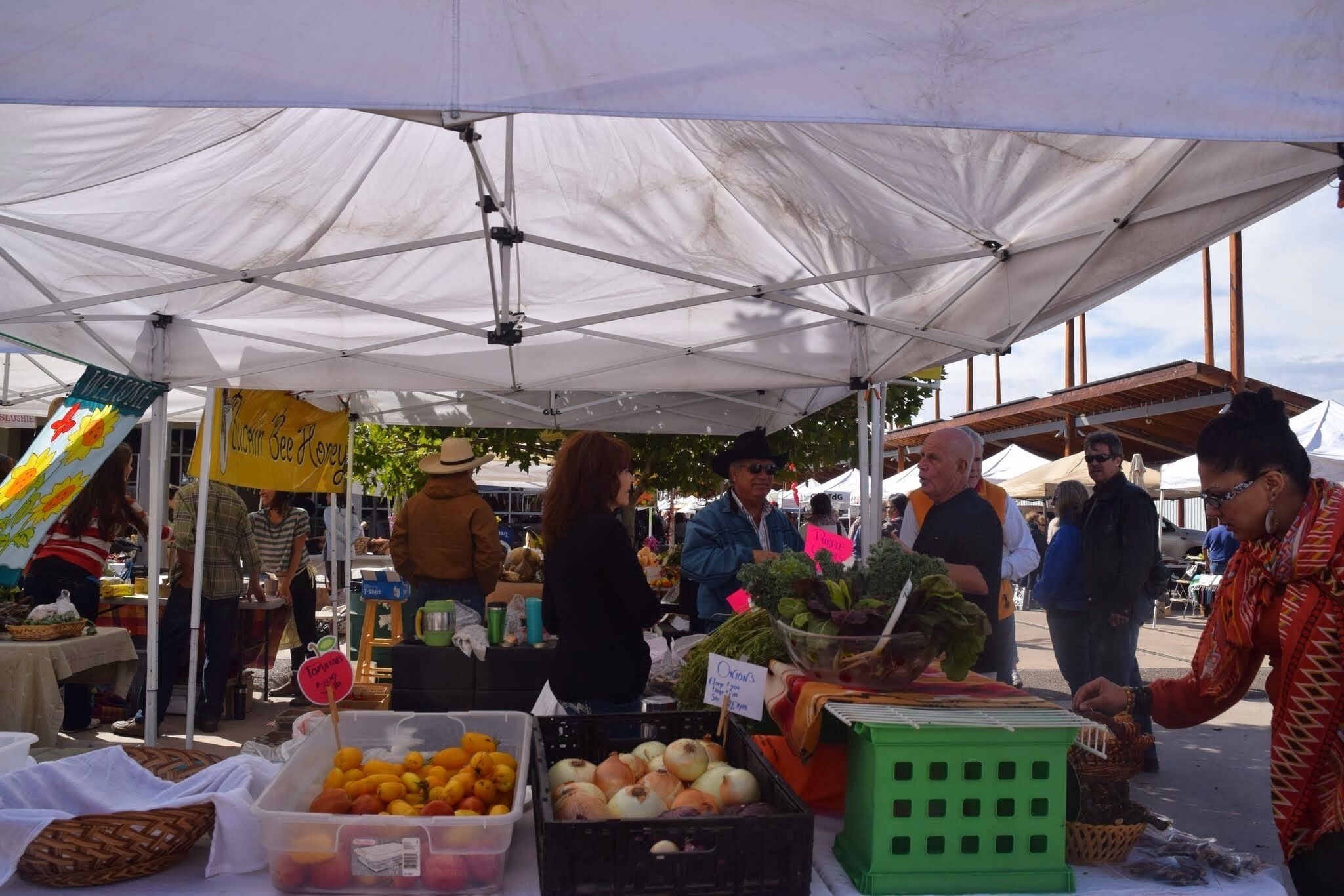 Un puesto de mercado con diversas frutas y verduras bajo un toldo blanco.