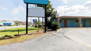 A parking lot with a large blank signboard, a building with multiple doors, and a clear sky. - Hotel O Kissimmee West - US 192 (Kissimmee)