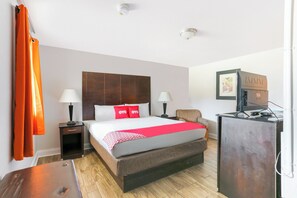 Habitación de hotel con una cama grande, dos mesitas de noche con lámparas, un escritorio con computadora y una televisión.