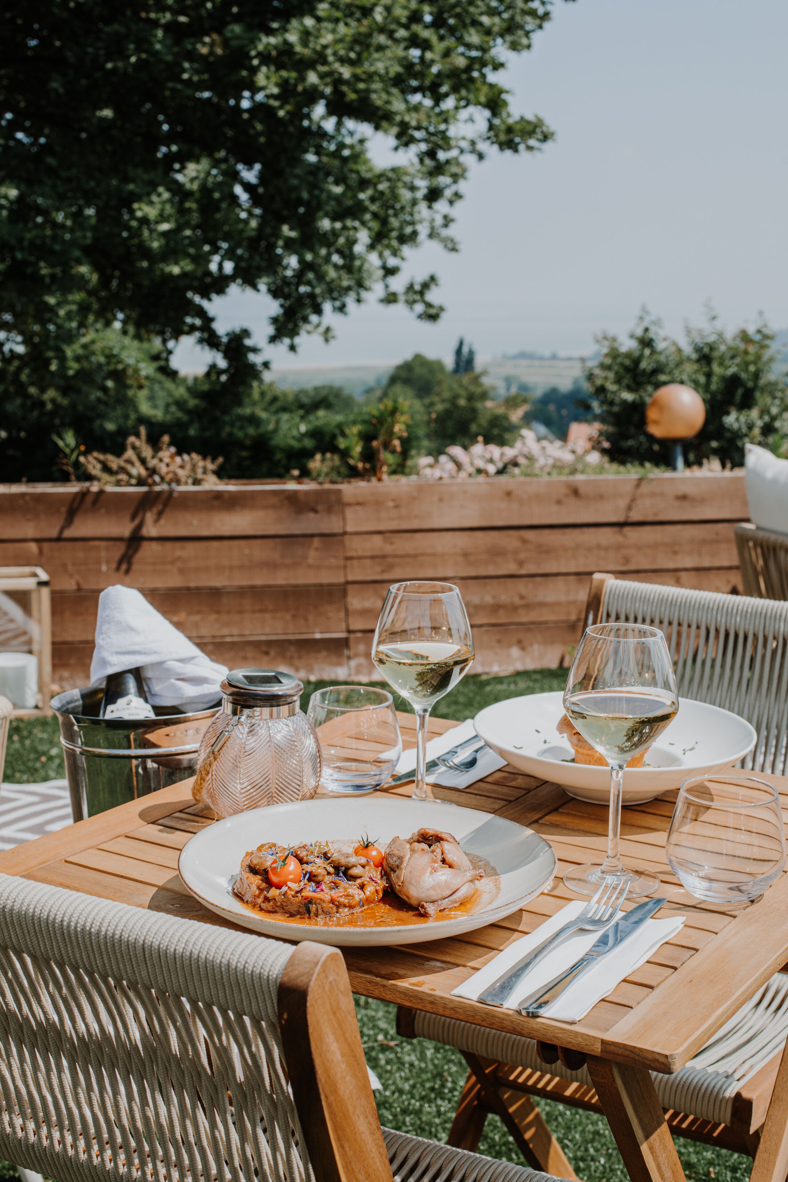 Mesa para comer al aire libre con comida, copas de vino y cubiertos.