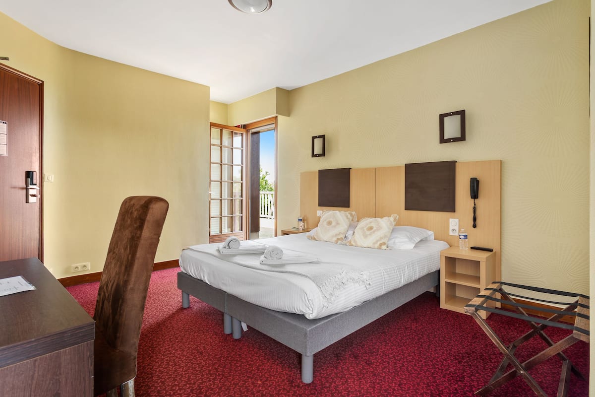 A hotel room with a bed, a desk, a chair, a nightstand, and a window.