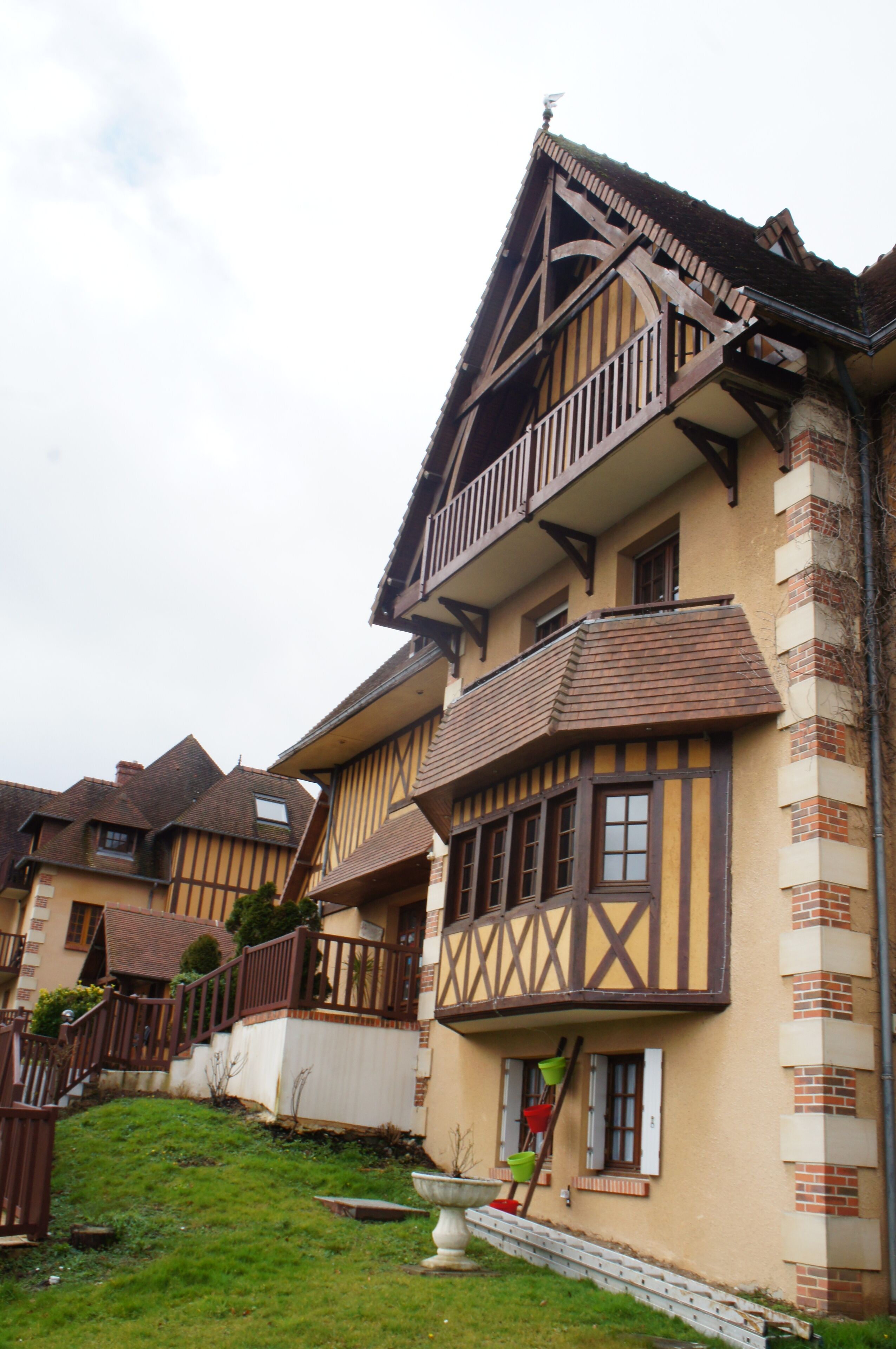A traditional half-timbered house with a balcony, a small garden, and a visible staircase leading to the entrance.