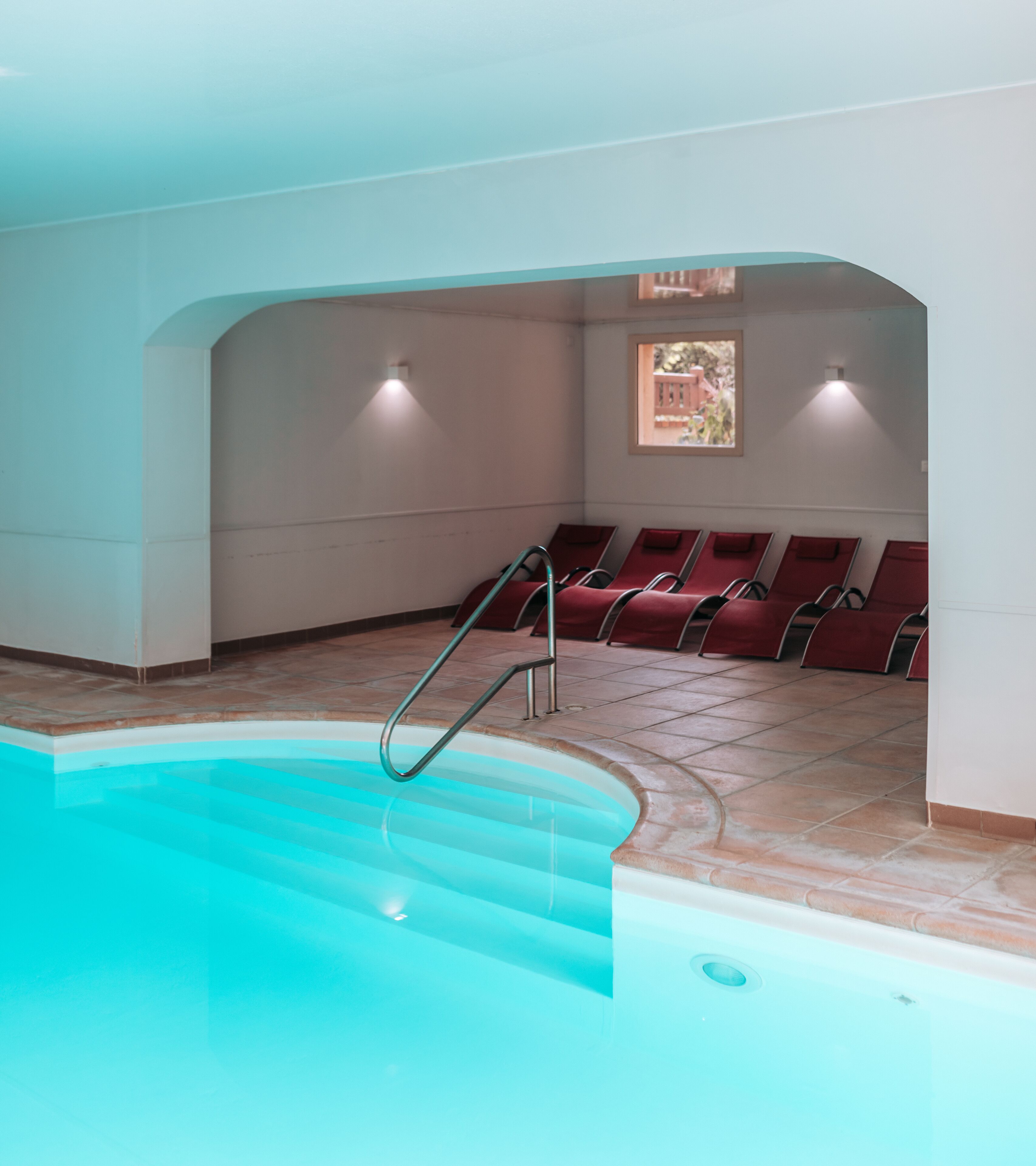 Une piscine avec des marches permettant d’y accéder, entourée de chaises rouges et dotée d’un sol carrelé.