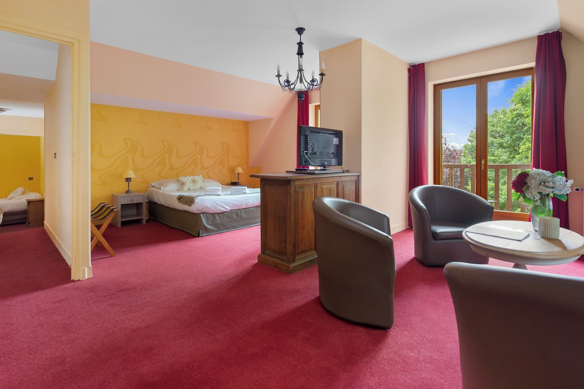 A hotel room with a bed, a TV on a wooden stand, a balcony with a chair, and a table with a vase.