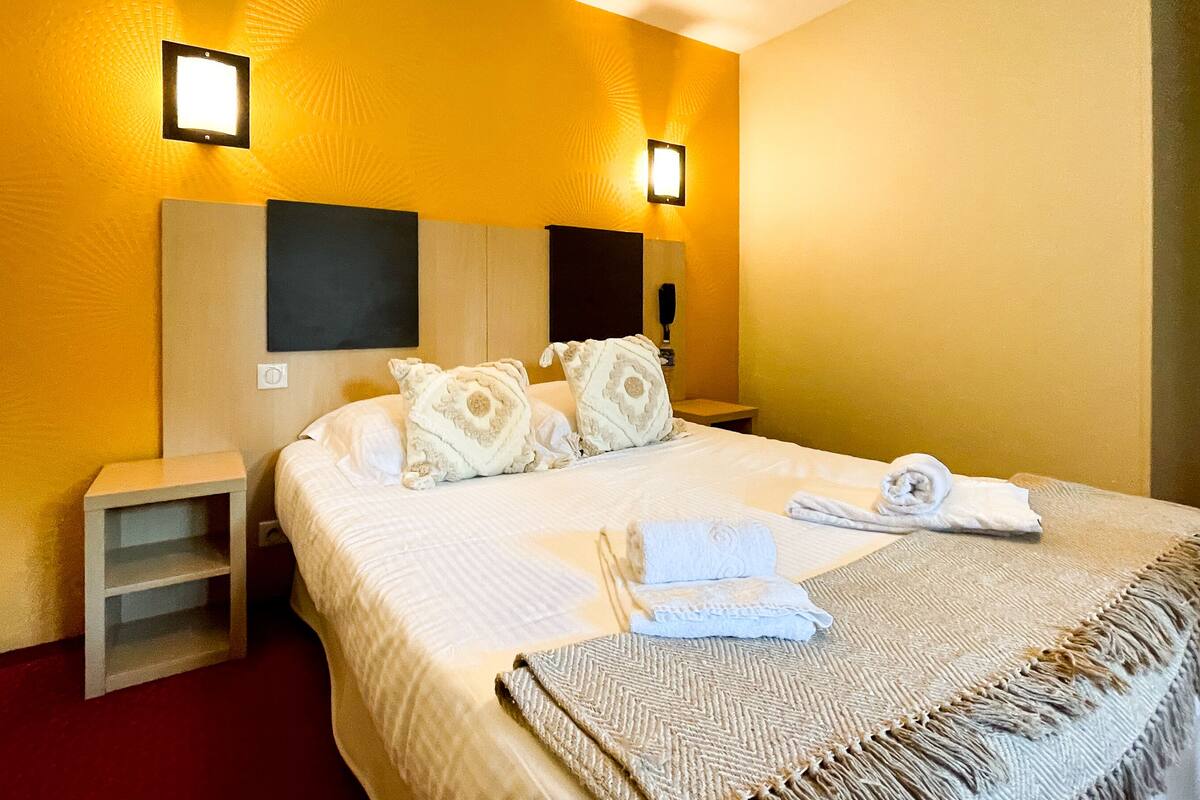 A hotel room with a large bed, two bedside tables, and two wall-mounted lights.